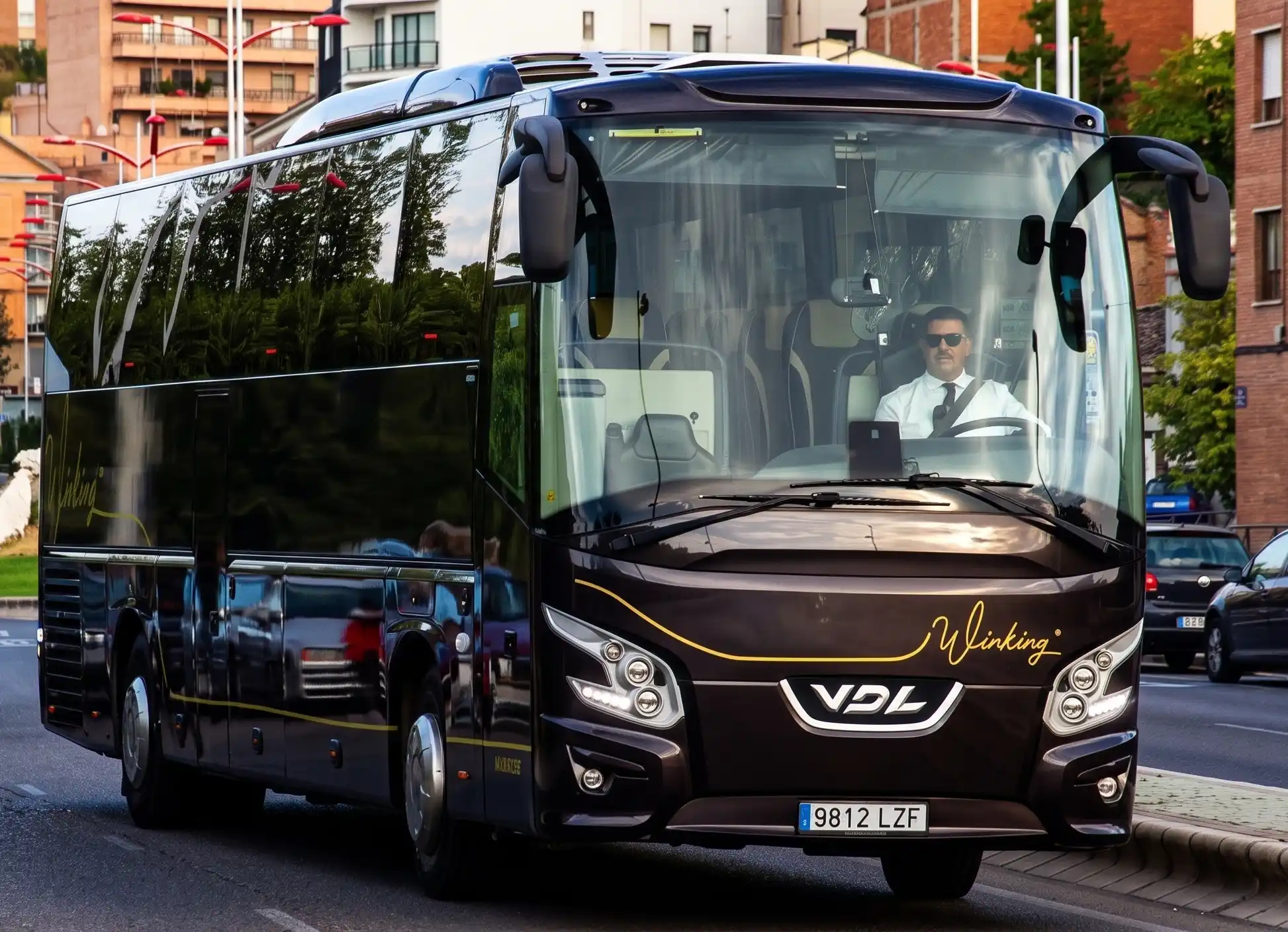 Dos autocares VDL negros de Winking Bus circulando por una calle de ciudad, con el conductor de camisa blanca al volante del primero