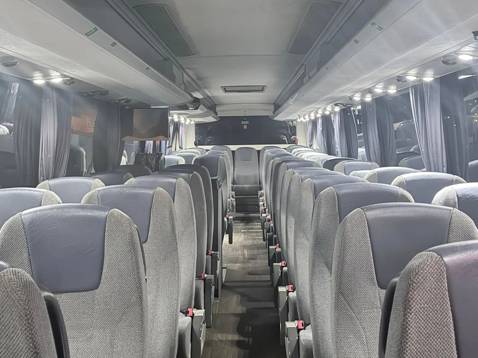Pasillo central del autobús VDL de 55 plazas de Winking Bus, con butacas reclinables grises de cabecero azul, cortinas y luces de lectura encendidas