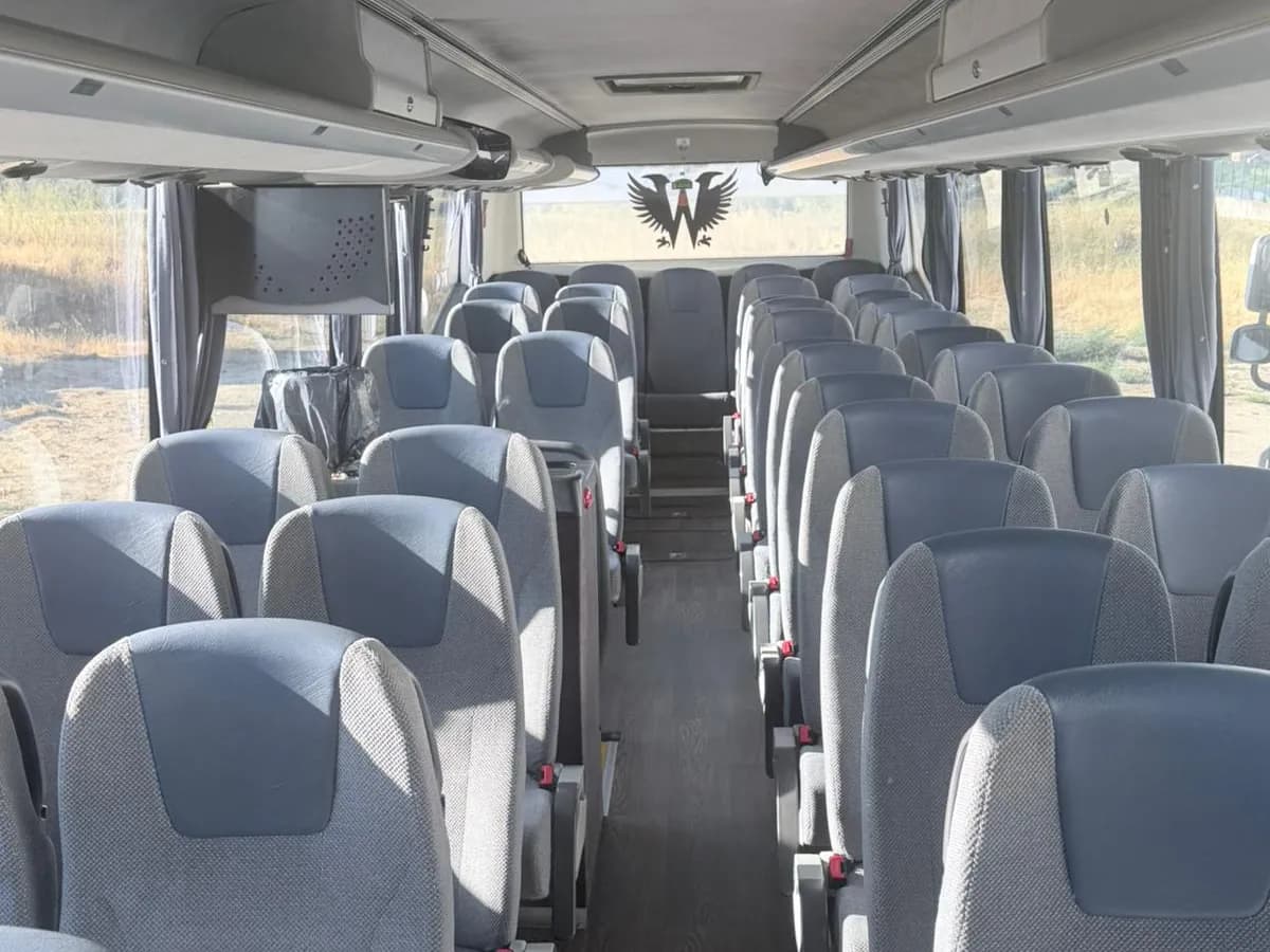 Pasillo central del autobús VDL de 70 plazas de Winking Bus, con las filas de butacas grises de cabecero azul y el logotipo de Winking en la mampara delantera