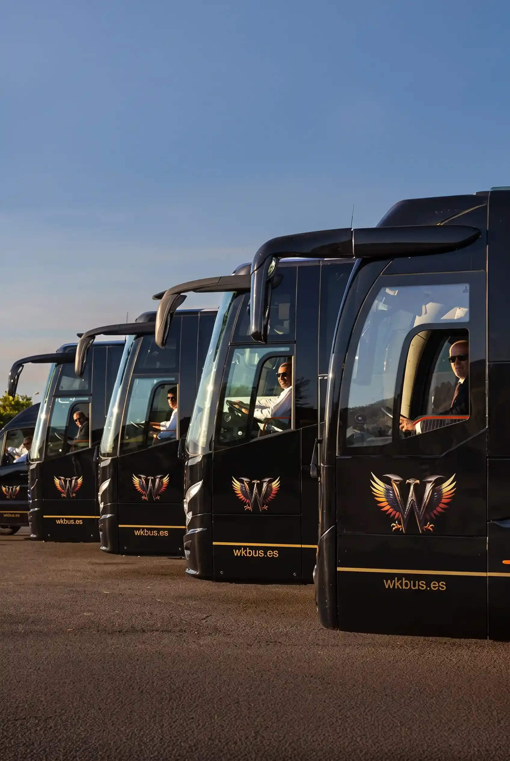 Cinco autocares de Winking Bus en fila con sus conductores de traje al volante