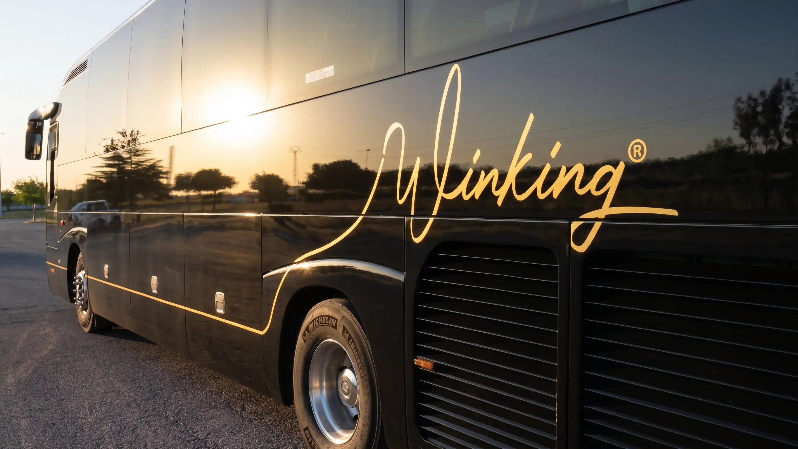 Lateral de un autocar negro de Winking Bus con el rótulo dorado, a contraluz al atardecer