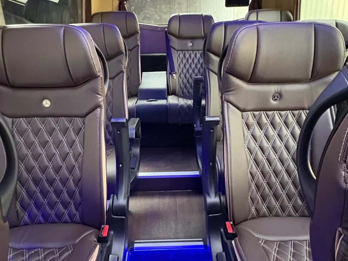Pasillo del microbús Mercedes-Benz Sprinter de 19 plazas de Winking Bus, con butacas de piel oscura acolchadas en rombo y luz ambiente azul en el suelo
