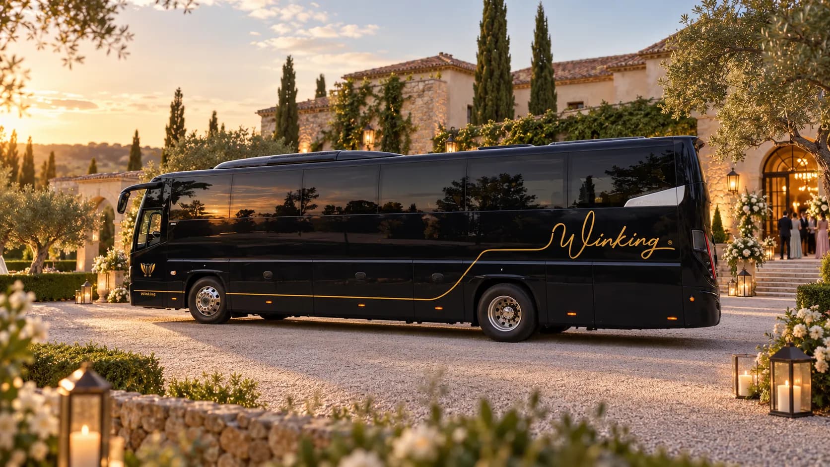 Autocar negro de Winking Bus con el rótulo Winking en dorado a la entrada de una finca de bodas al atardecer, con flores blancas y faroles