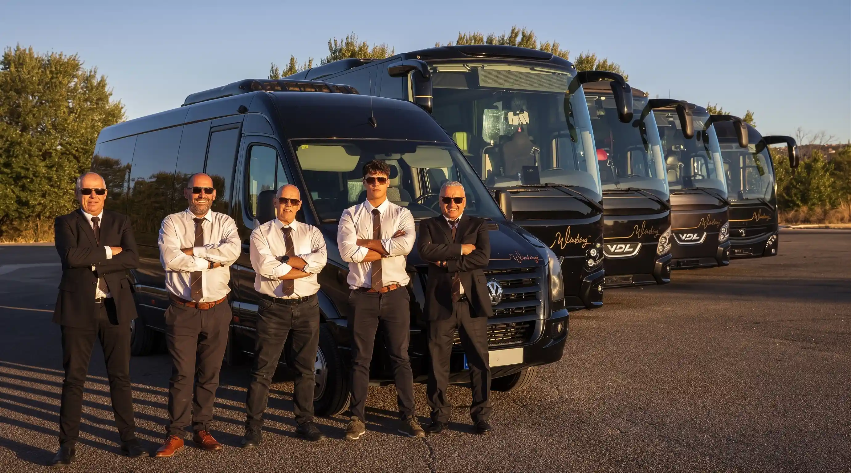 Los conductores de Winking Bus, de traje y corbata marrón, frente al microbús y los autocares de la flota