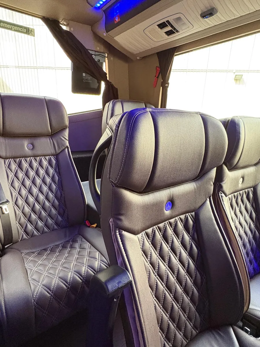 Butacas de piel oscura con tapicería capitoné de rombos y costuras claras en el microbús Sprinter de Winking Bus, con luz azul en el techo